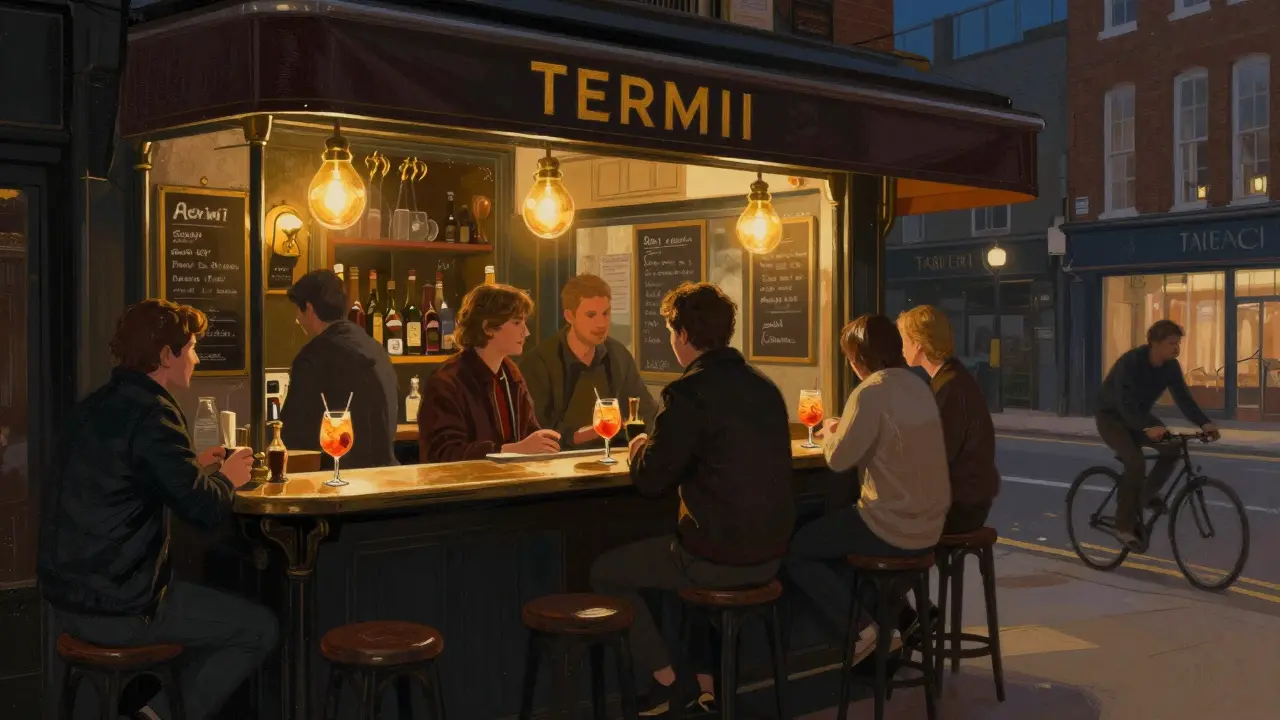 Cozy Bar Termini in Shoreditch at night, patrons standing at counter with Aperol Spritzes, warm interior lighting.